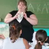 Illusztráció: tanárnő a zöld tábla előtt, kezében könyvvel, figyelő gyermekek fejei az előtérben